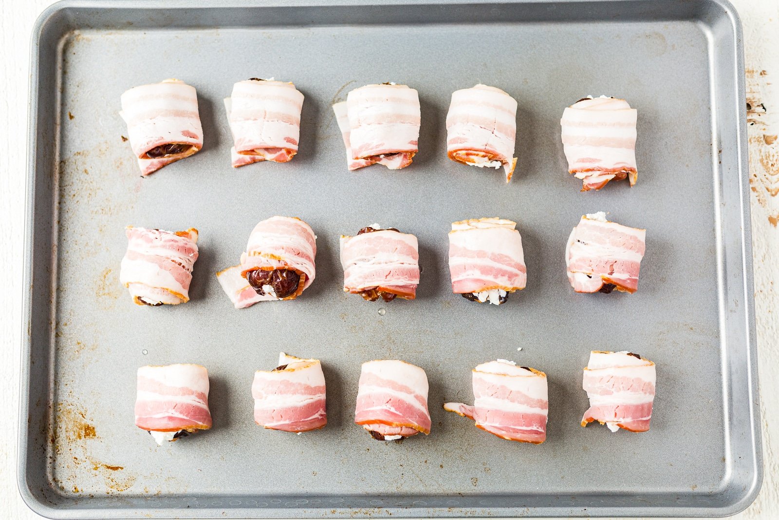 bacon wrapped dates with goat cheese on a baking pan before cooking.