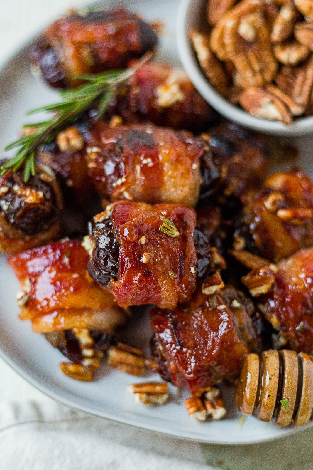 bacon wrapped goat cheese dates on a plate with honey glaze and pecans.