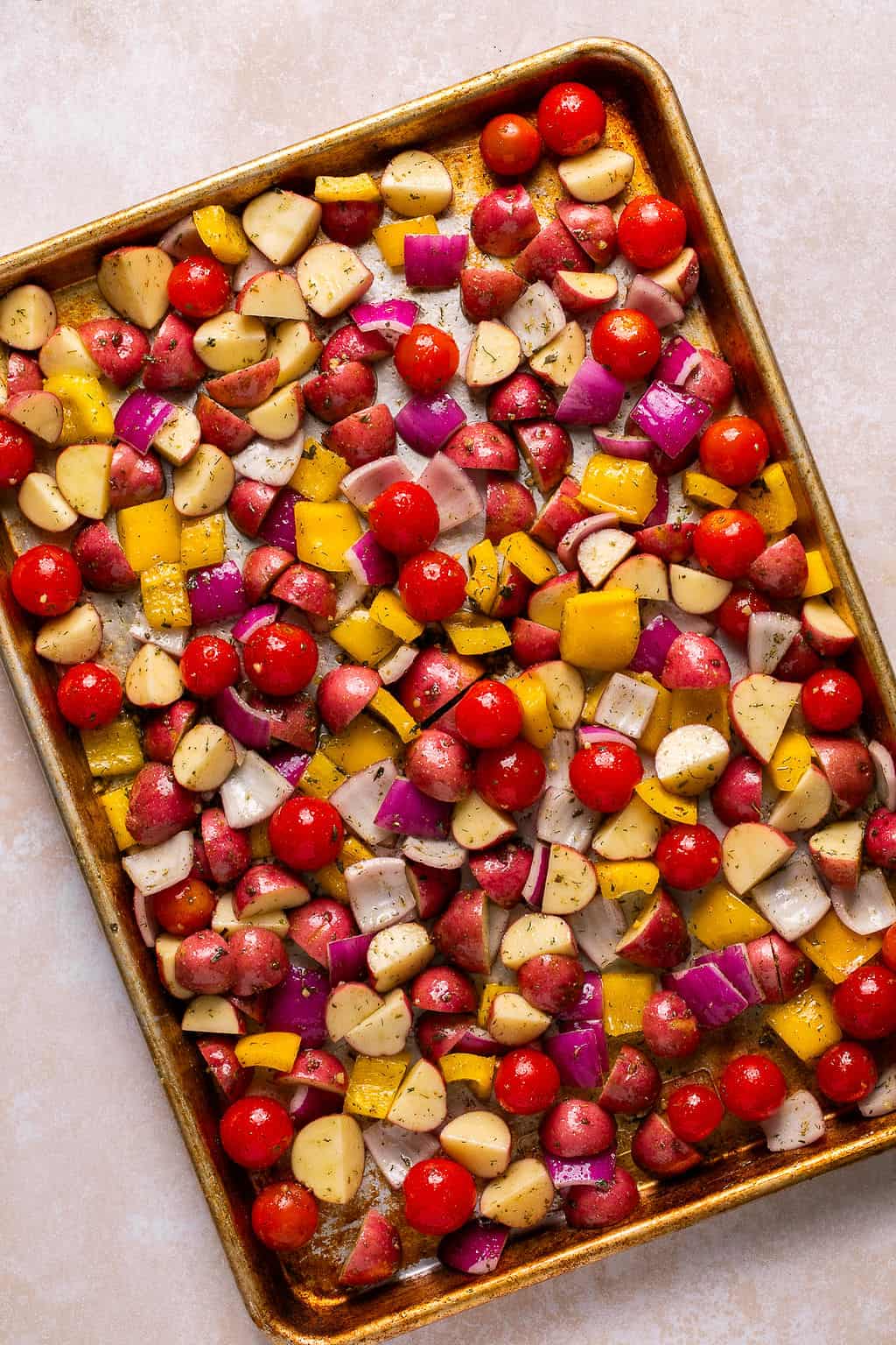 vegetables tossed in greek seasoning and olive oil on a sheet pan