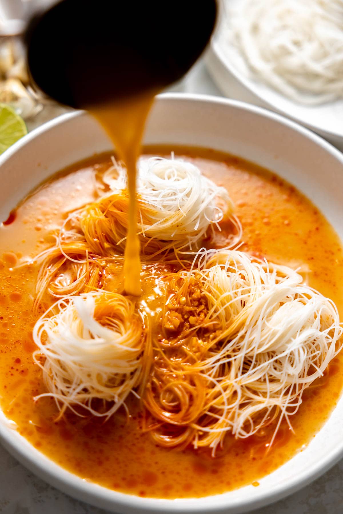 pouring coconut curry broth over rice noodles