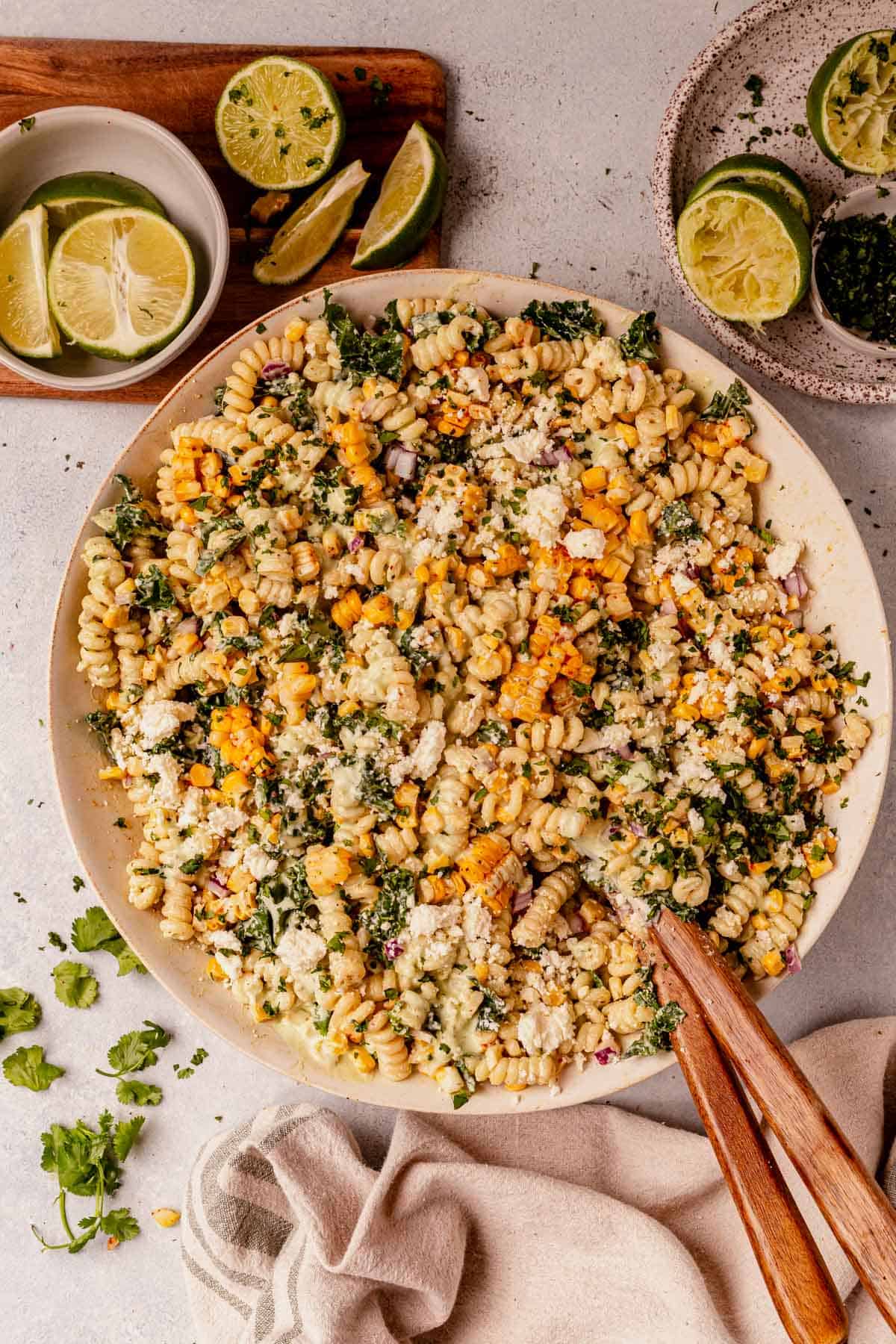 Mexican street corn pasta salad in a ceramic bowl with wood spoon and lime garnish