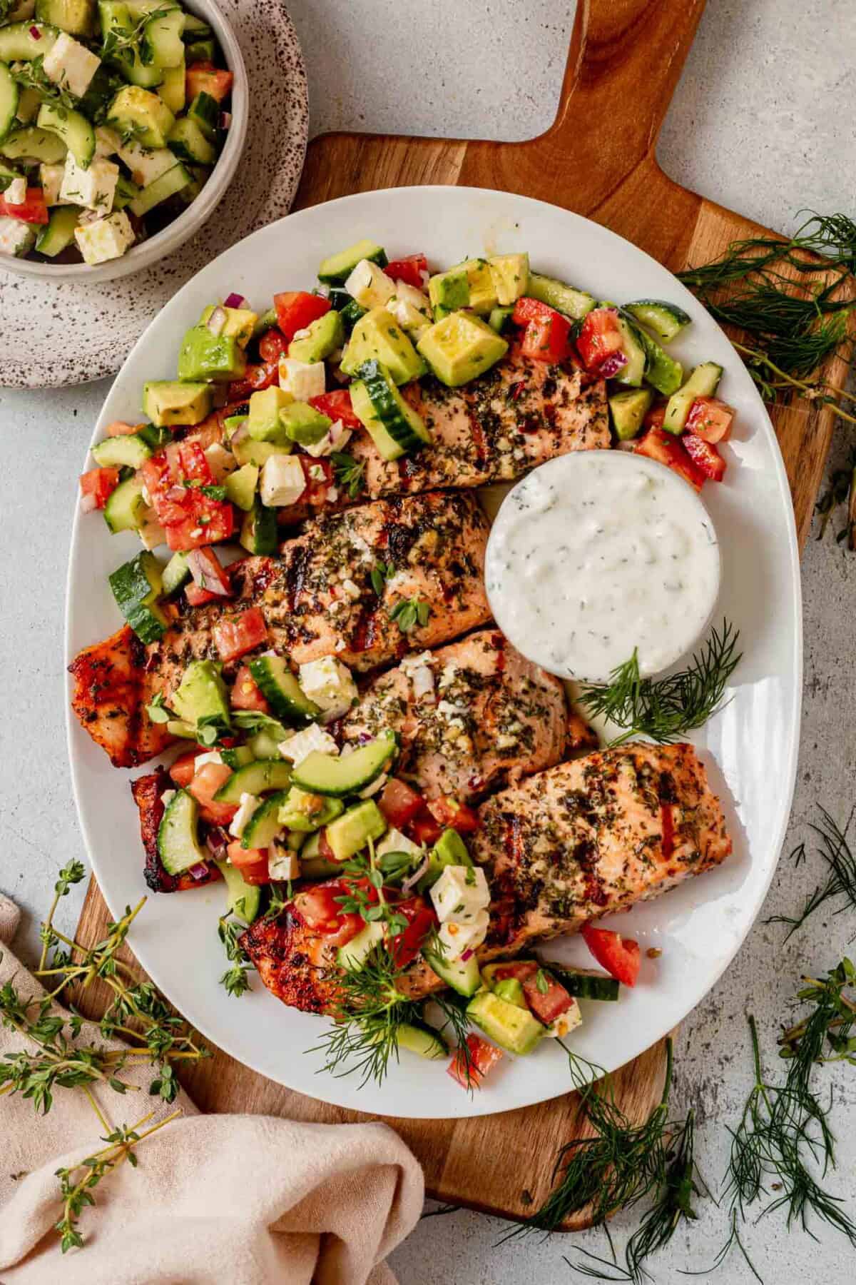 greek salmon on a platter with greek salad and tzatziki on the side