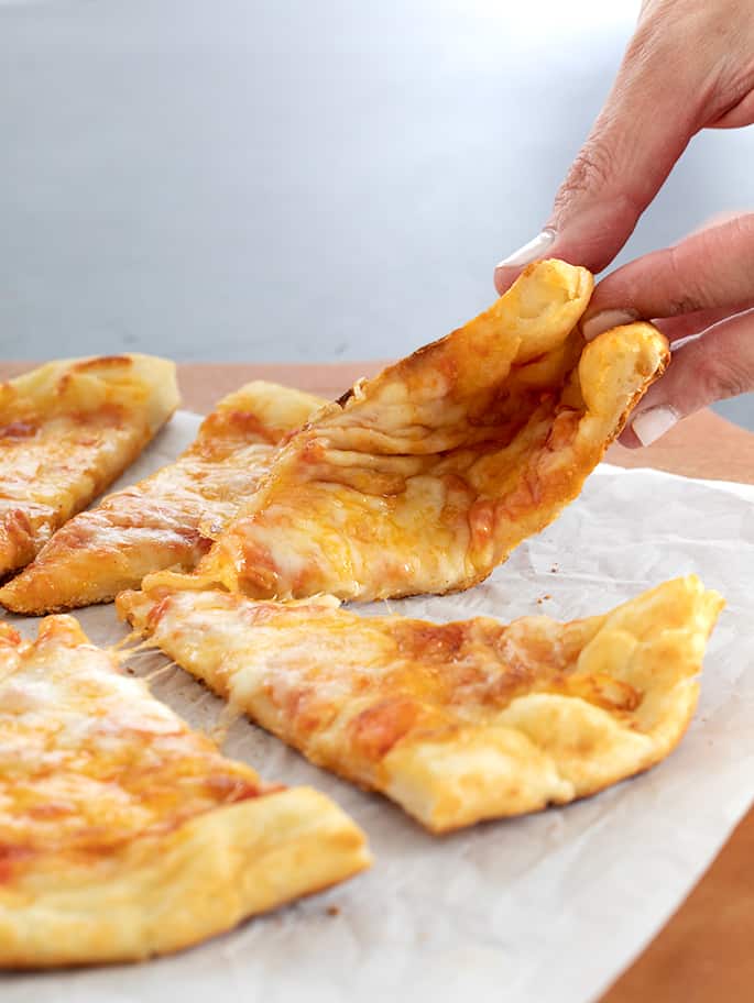 Fingers folding a piece of NY style pizza in a pie of slices