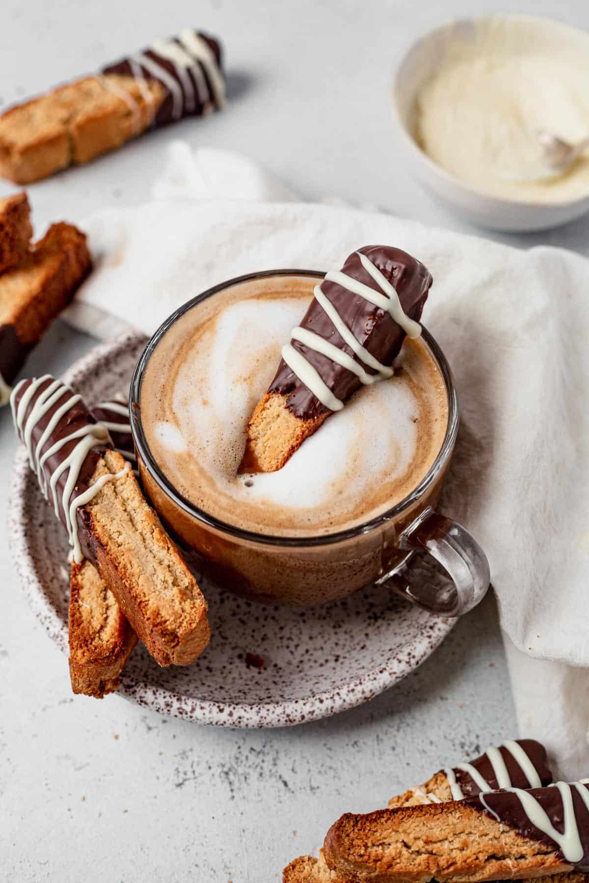 gluten free biscotti dipped in chocolate dunked into a cappuccino in a small glass mug