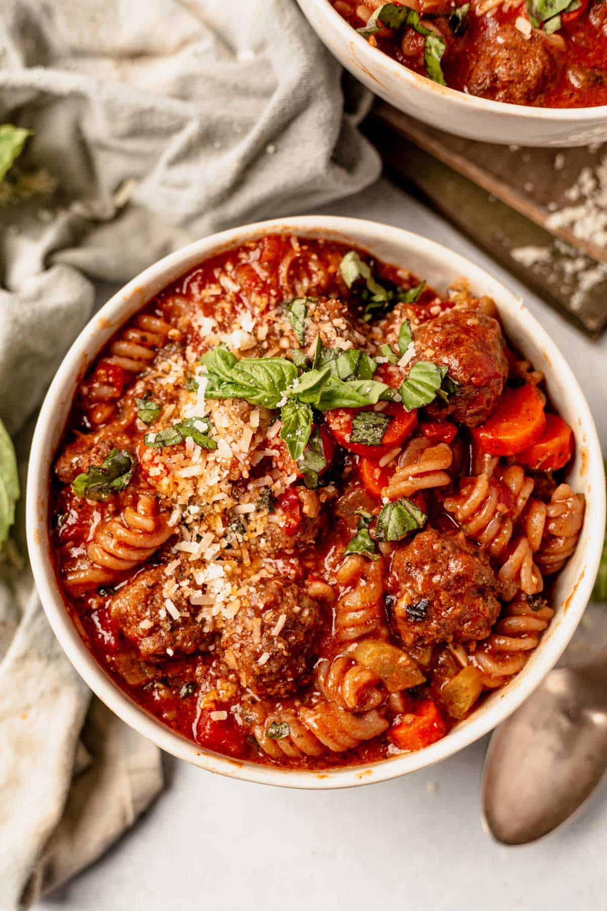 a bowl of italian meatball soup with parmesan and basil