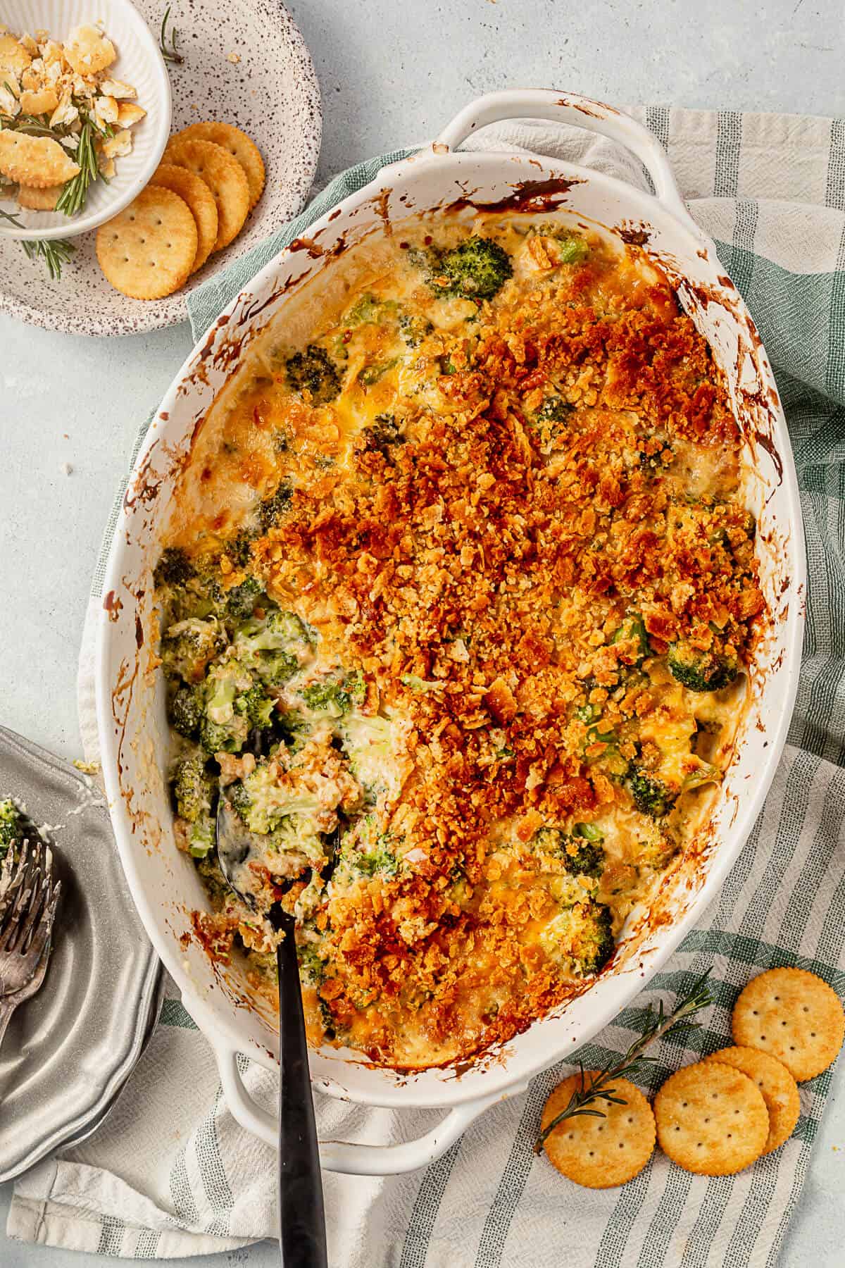 a serving spoon resting in broccoli casserole with a scoop taken out on a plate next to it