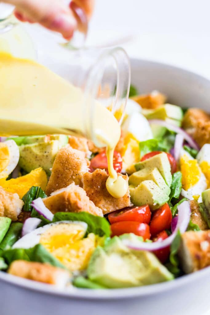 honey mustard dressing being poured on crispy chicken salad