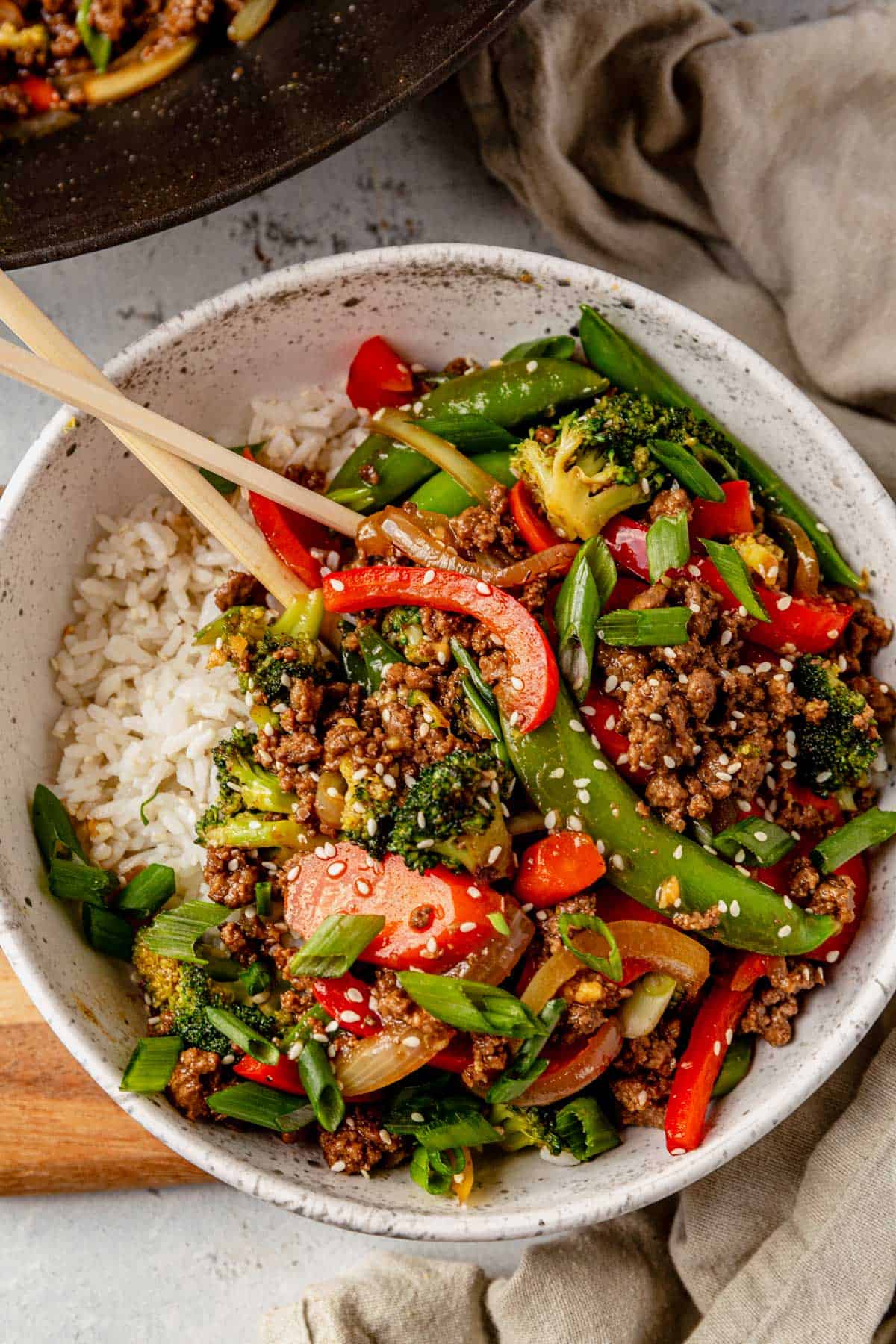 a bowl of ground beef stir fry over rice with chopsticks