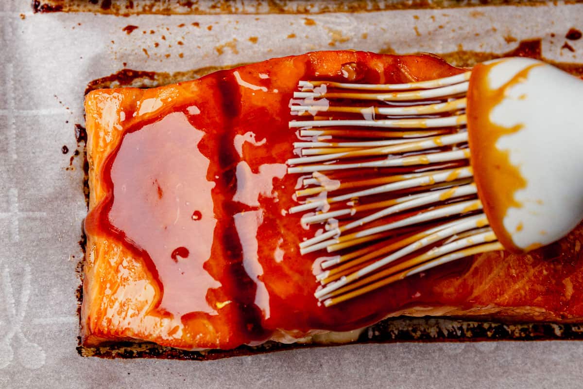 brushing honey sriracha glaze on cooked salmon