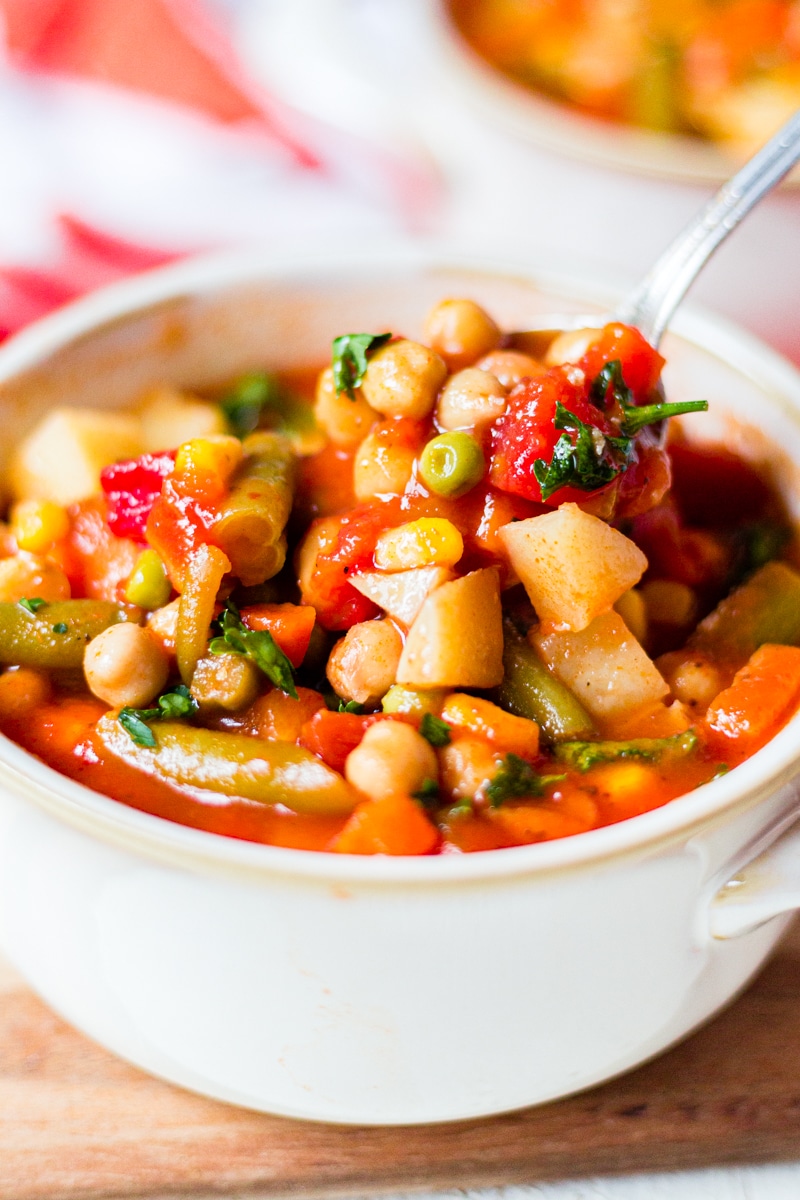 A spoon scooping out vegetable soup with fresh parsley on top