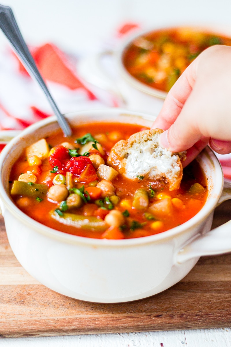 dipping buttered bread into a bowl of hot vegetable soup