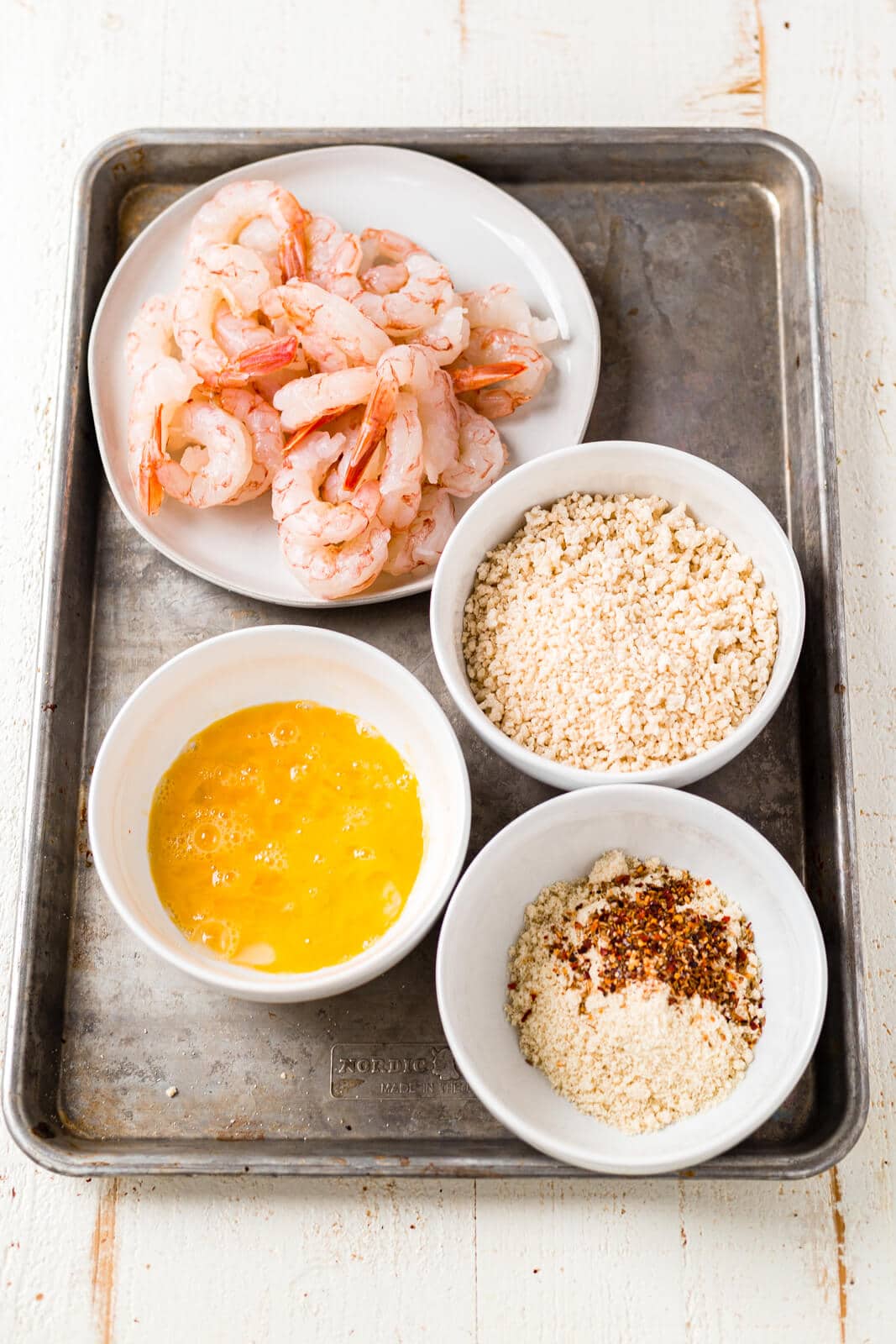 all of the ingredients for breaded shrimp in the air fryer shrimp sitting on a sheet pan before being breaded and cooked