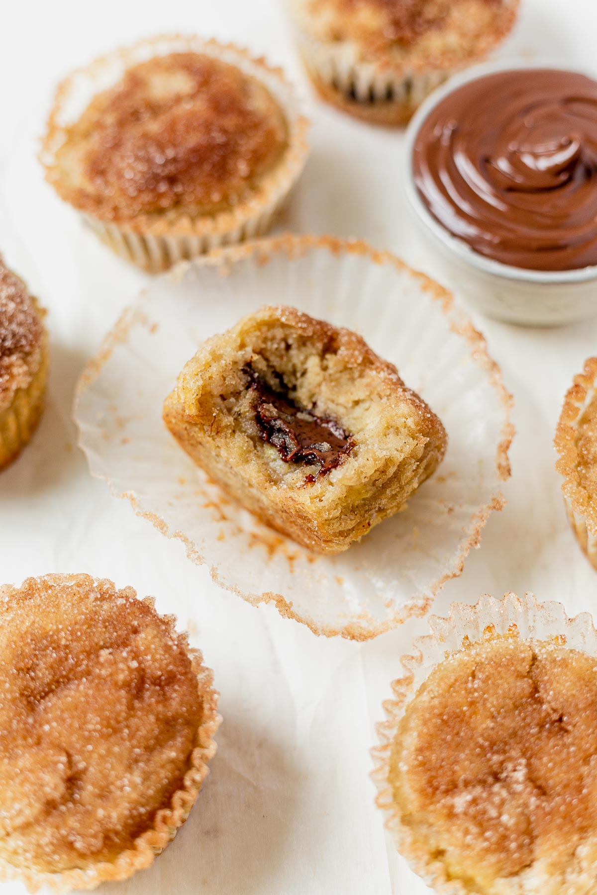 a banana nutella muffin with a bite taken out sitting inside a paper muffin liner with more muffins surrounding it