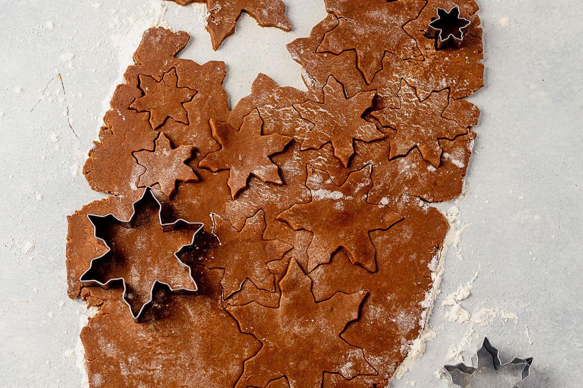 snowflake cookie shapes being cut out of cookie dough