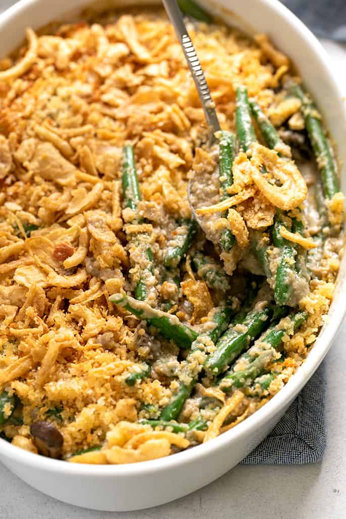 Serving spoon with spoonful of gluten free green bean casserole in white casserole dish