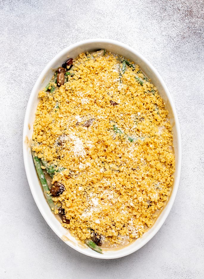 Overhead image of unbaked gluten free green bean casserole with breadcrumb topping and some green beans and mushrooms visible