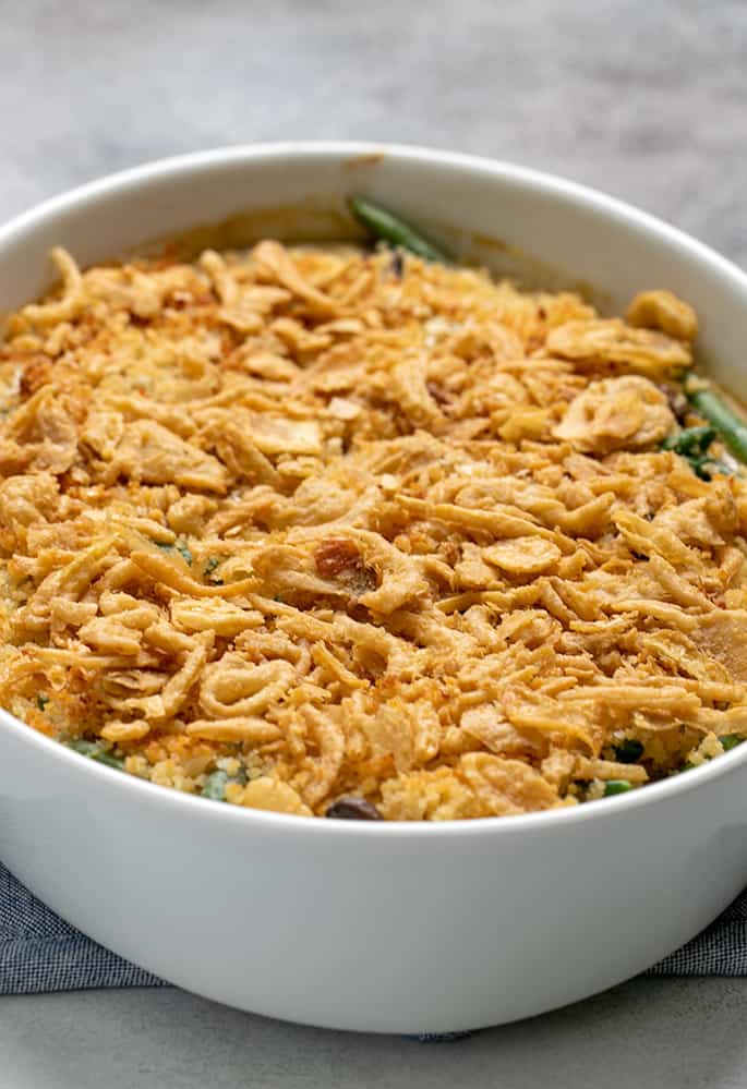 Baked green bean casserole with crispy fried onions on top in white casserole dish on blue potholder