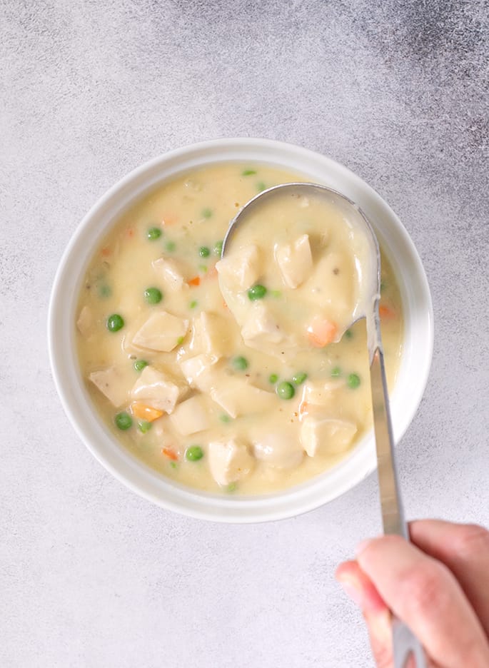 Ladle placing chicken pot pie filling into white casserole dish