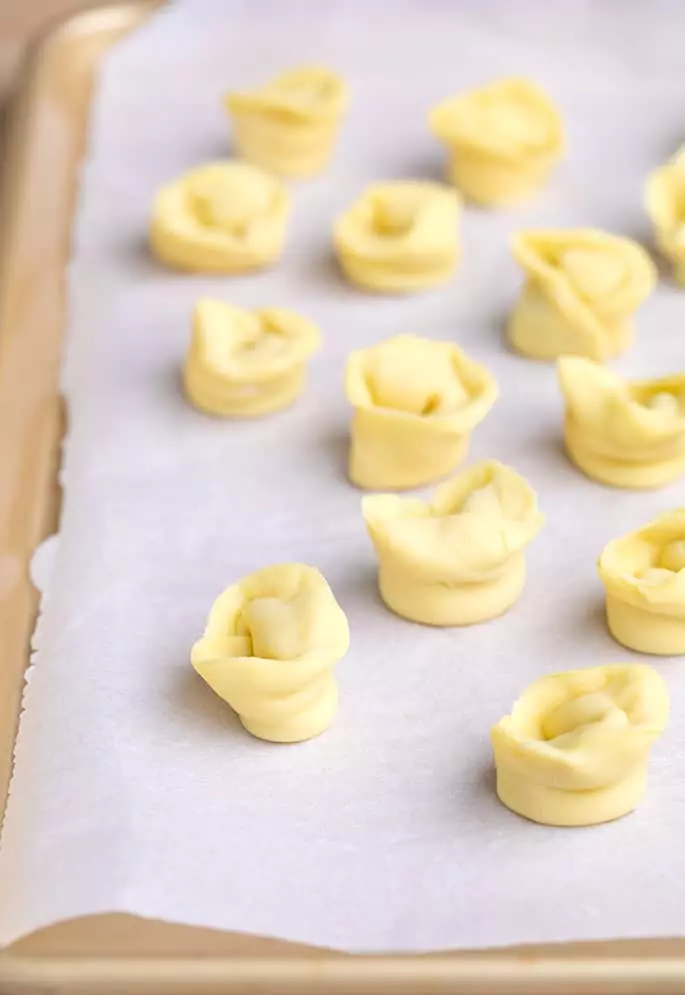 Raw shaped and filled tortellini pieces on white paper on tray