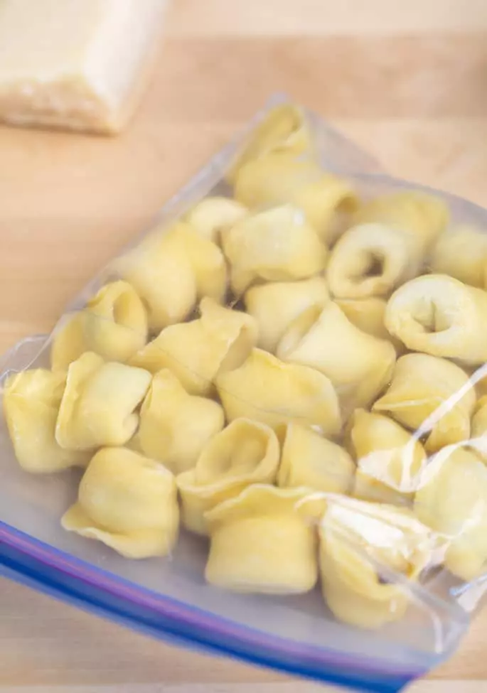 Shaped raw tortellini frozen in a zip top bag on a blond surface