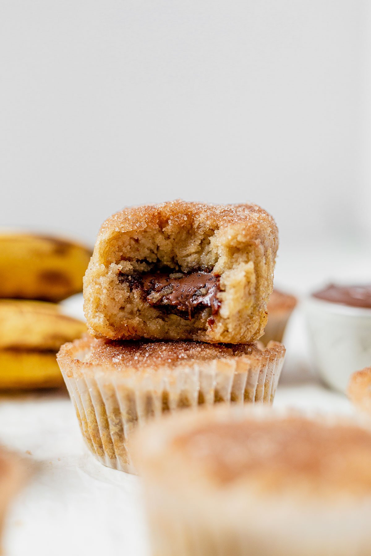 two banana nutella muffins stacked on top of each other and the top one has a bite taken out so you can see the gooey nutella inside