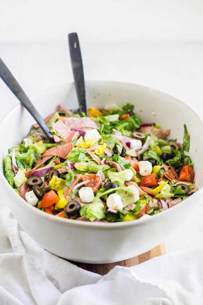 antipasto salad in a white serving bowl with black utensils