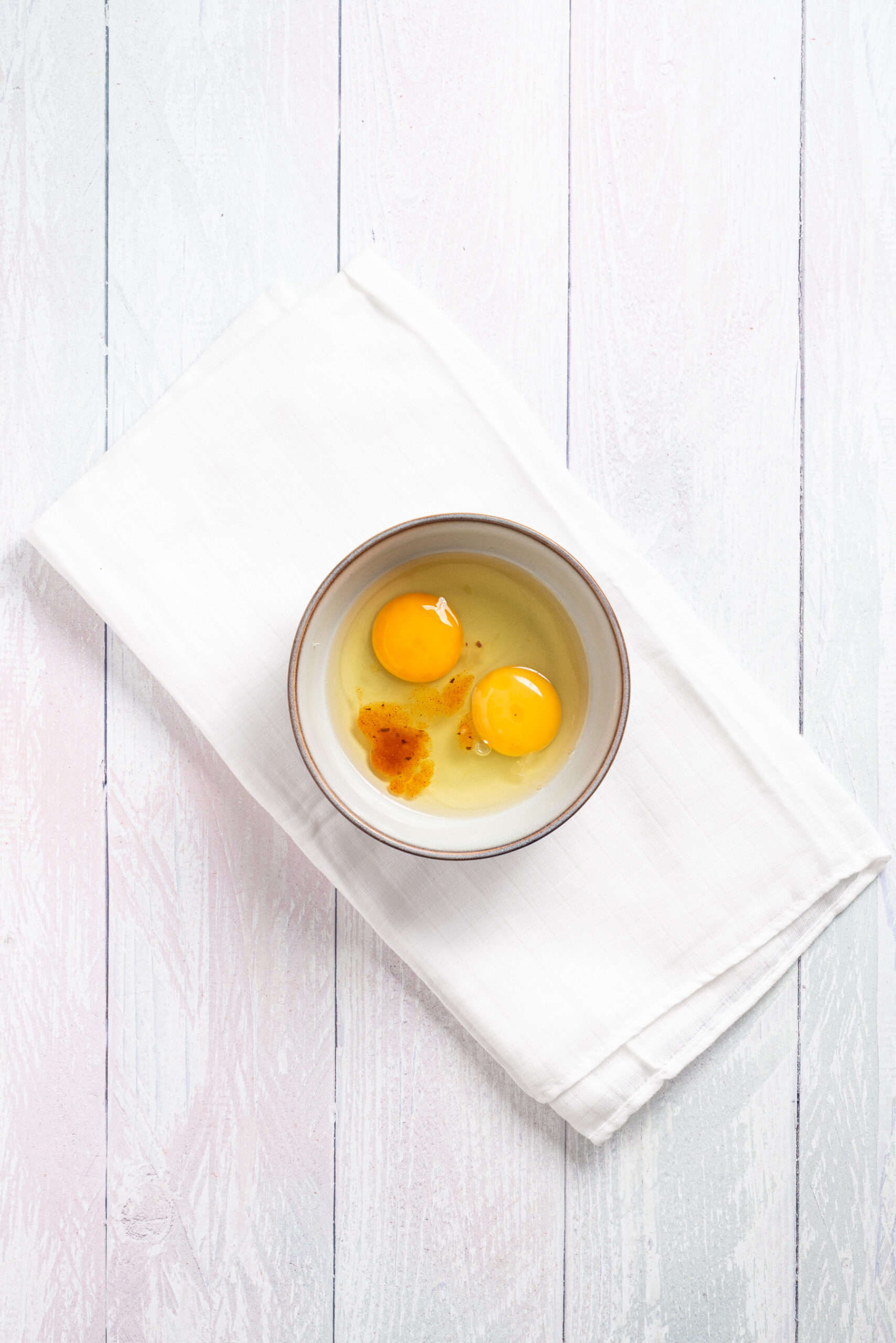 An overhead image of mixing two eggs with hot sauce and salt.