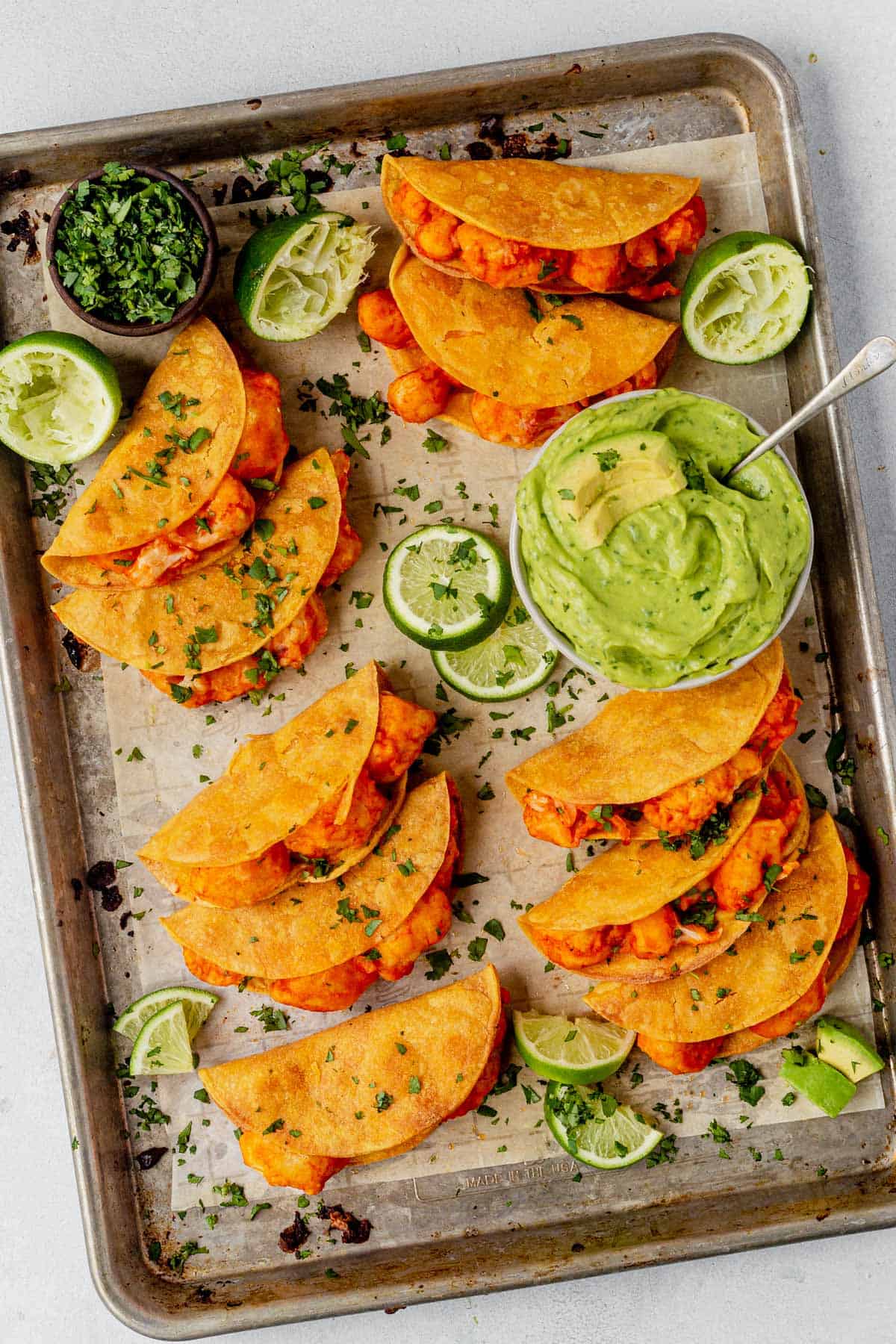 buffalo cauliflower tacos on a sheet pan with fresh lime and avocado crema