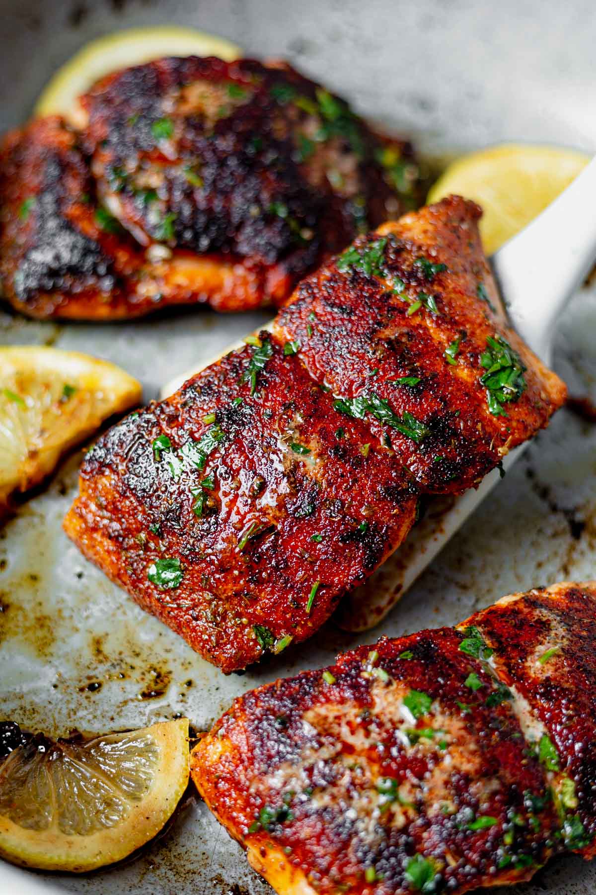 3 blackened salmon fillets in a skillet with lemon