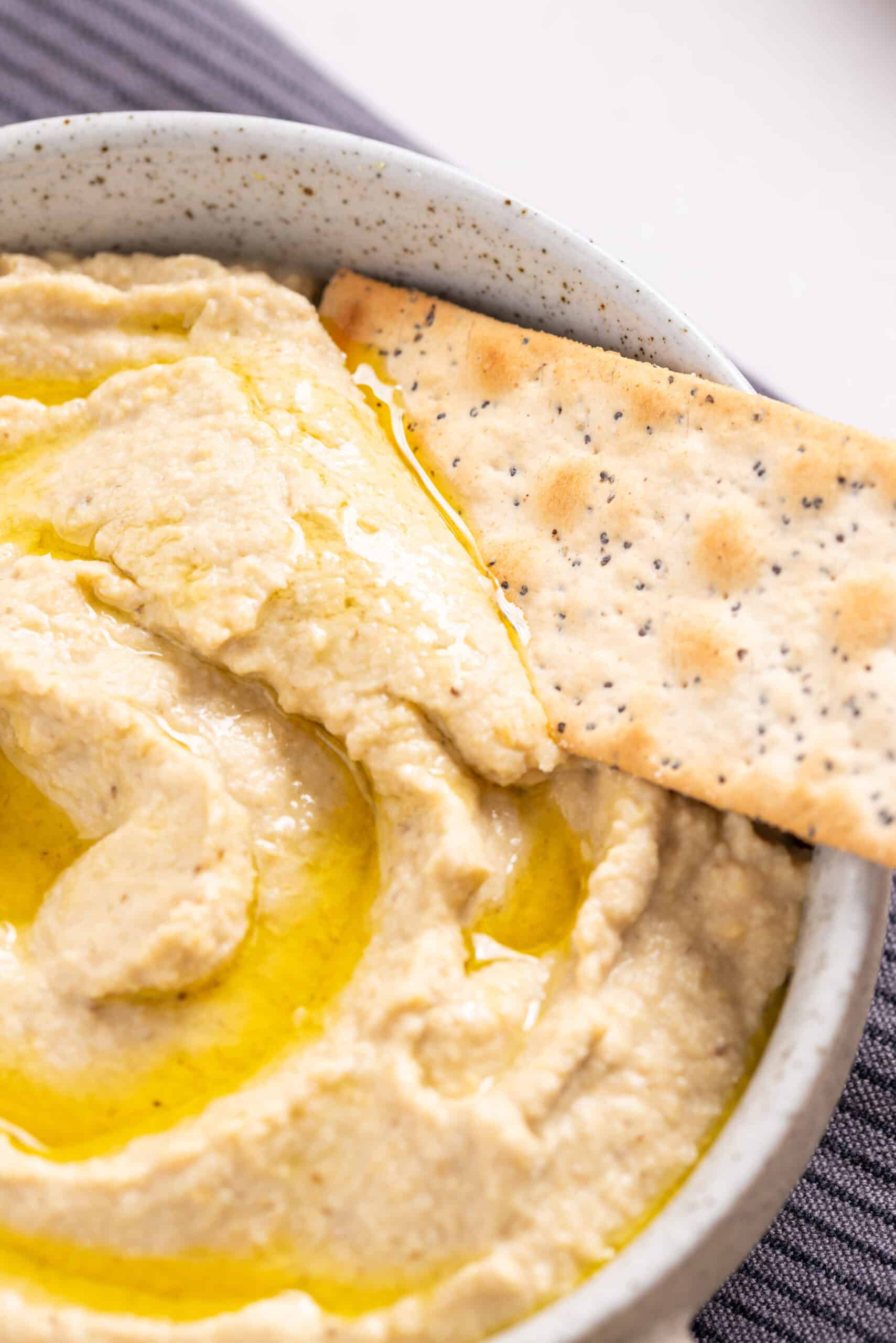 An image of scooping hummus with a cracker.