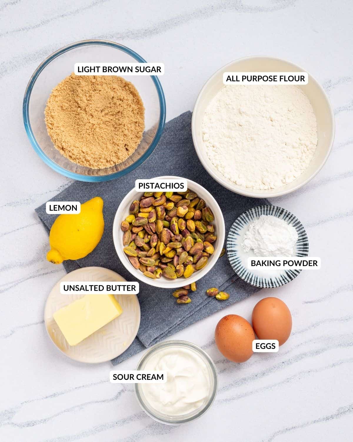 An overhead image of the ingredients of pistachio muffins in separate containers with labels.