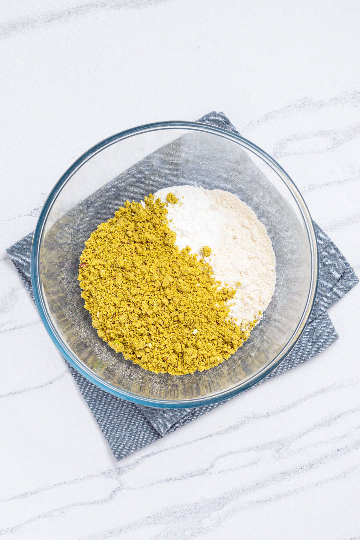 An image of pulverized pistachios in a bowl with flour, baking powder, and salt.