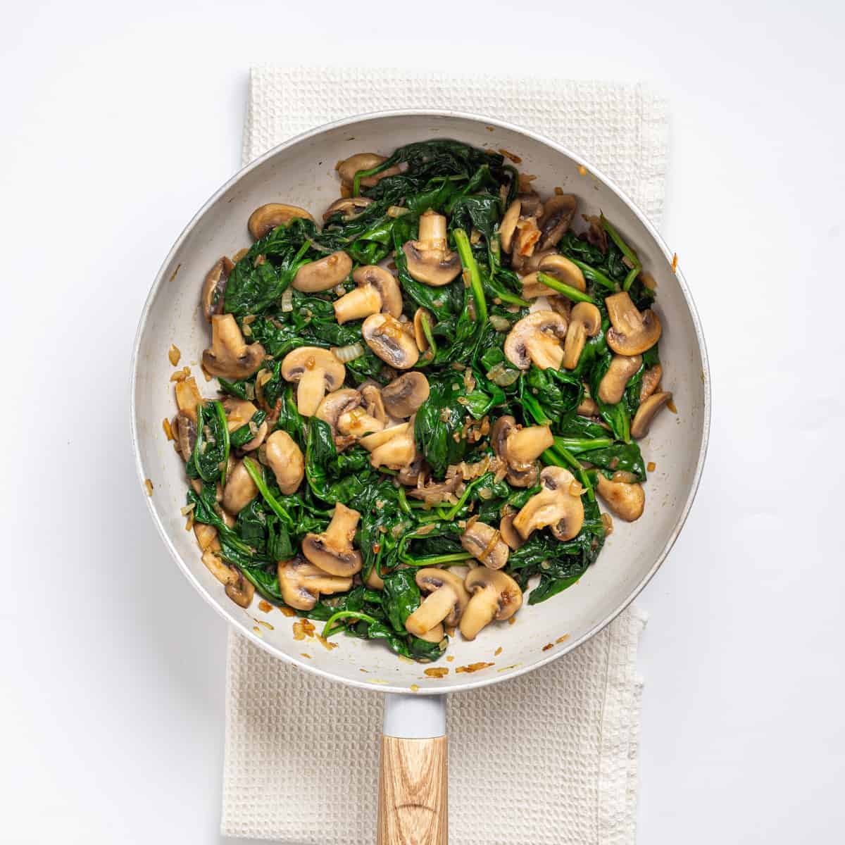 An overhead image of mushrooms, spinach, garlic, and onions cooked in a skillet.