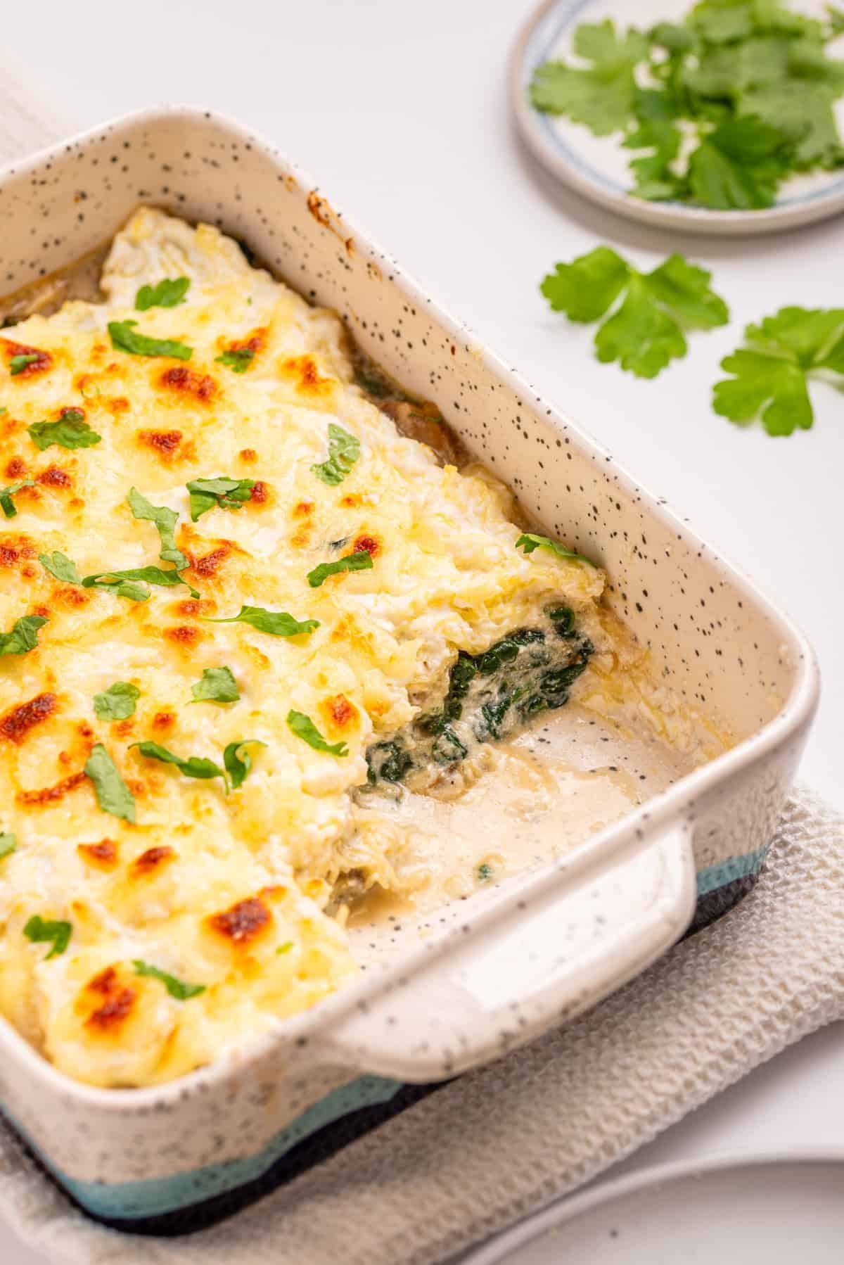 A close up image of spaghetti squash casserole with a serving missing from the lower right side of the baking dish.