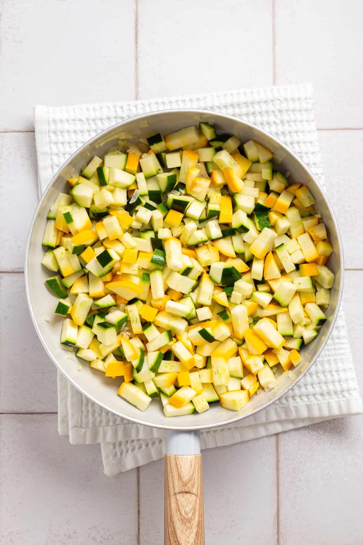 An overhead image of squash, zucchini, and onions in a large skillet.