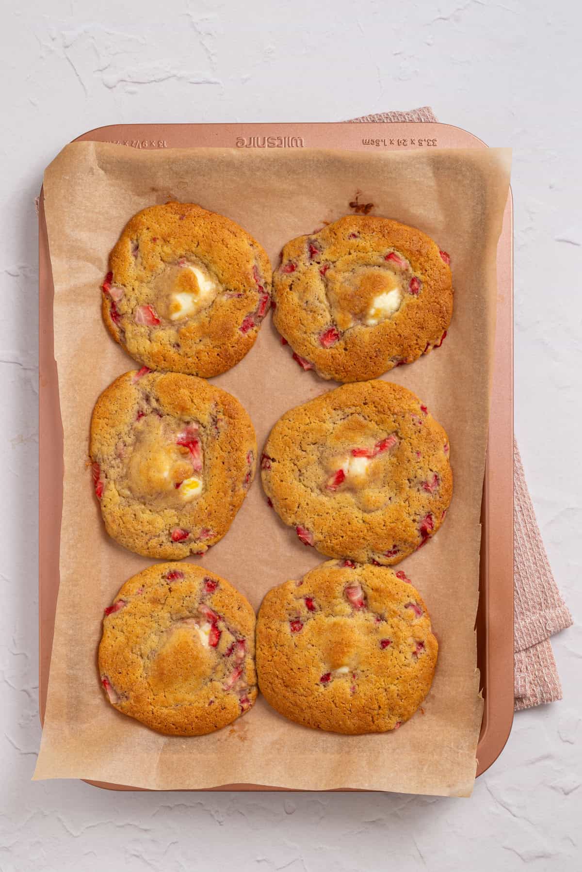 An image of freshly baked strawberry cheesecake cookies on a baking sheet.