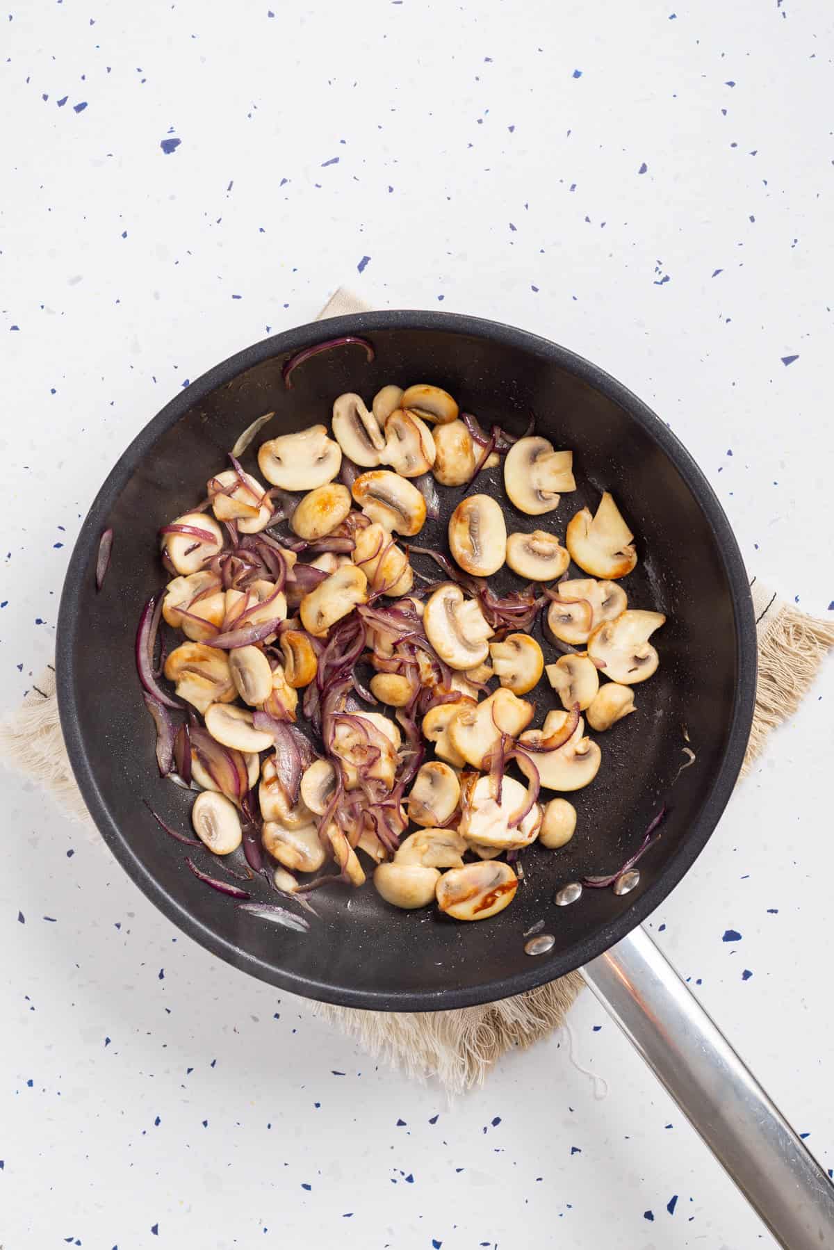 An overhead image of onion and mushrooms in a skillet.