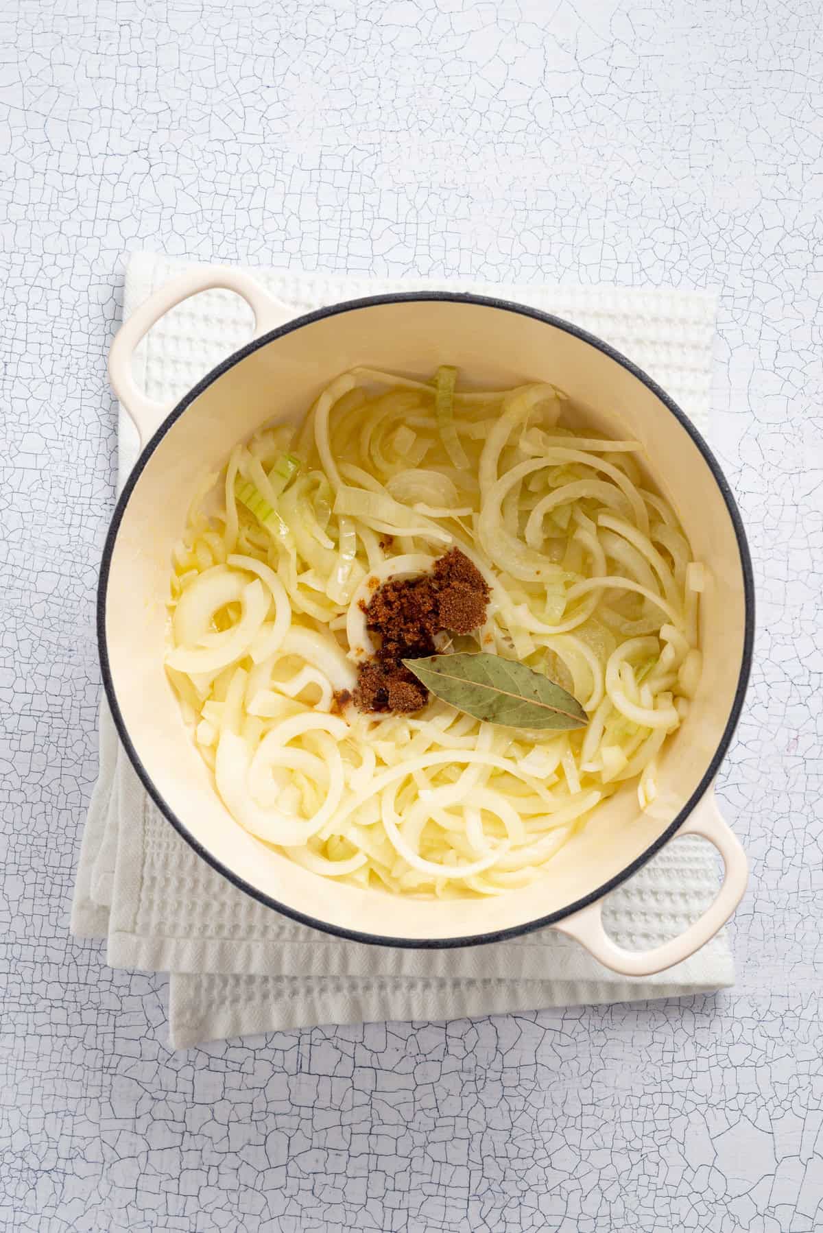 An overhead image of onions, brown sugar, and bay leaf in a dutch oven.