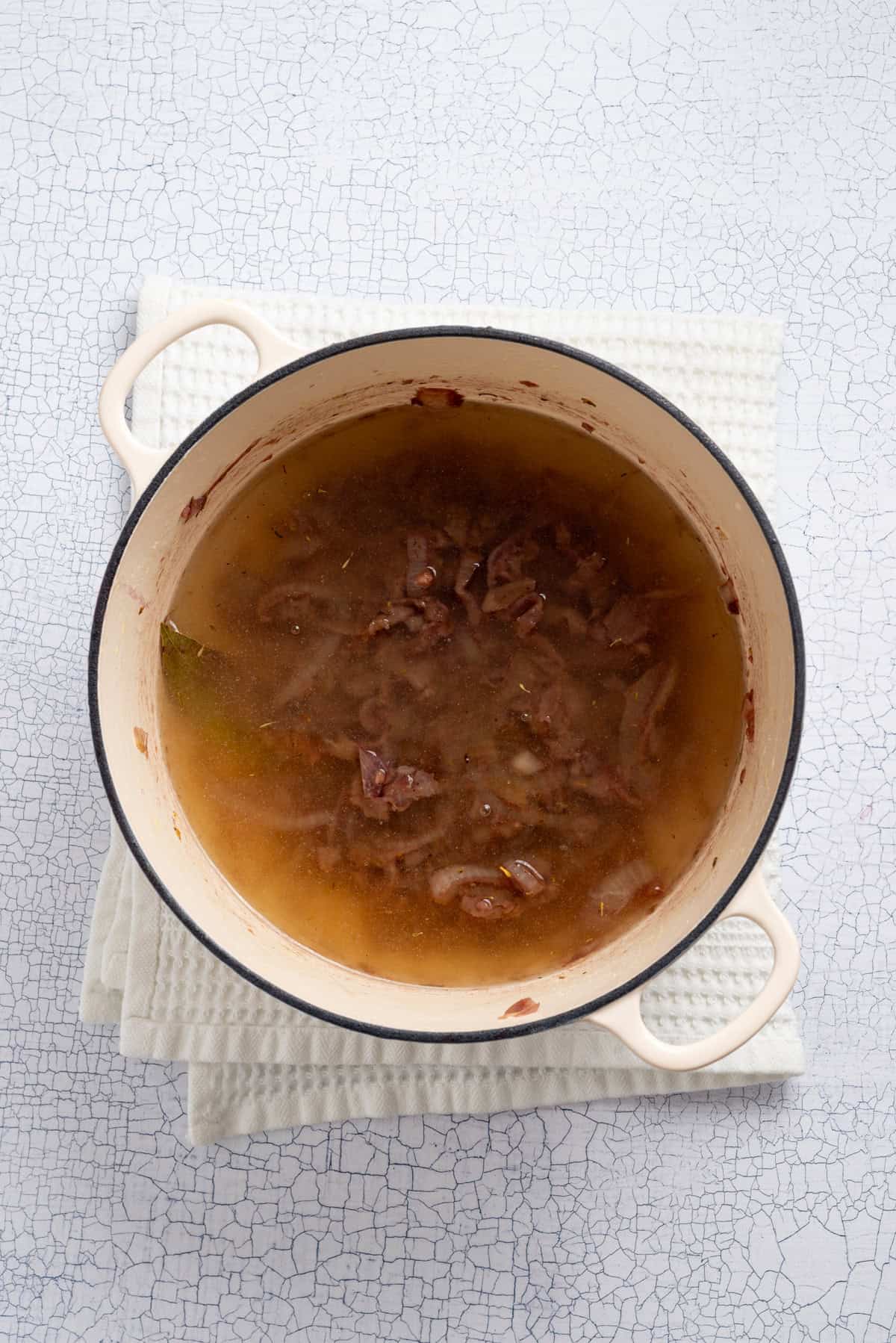 An overhead image of adding vegetable broth, salt, and pepper to the soup mixture.