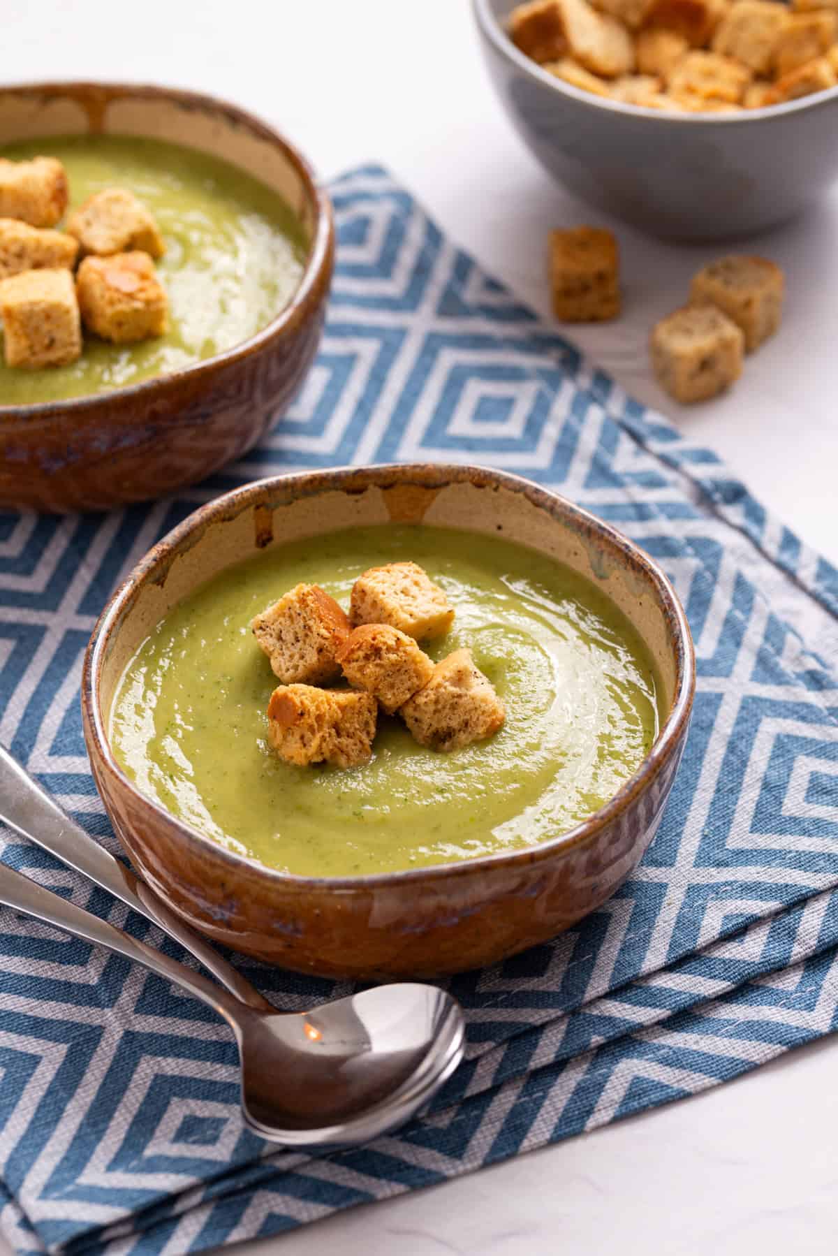 An image of zucchini soup in a bowl with a serving spoon on the side.