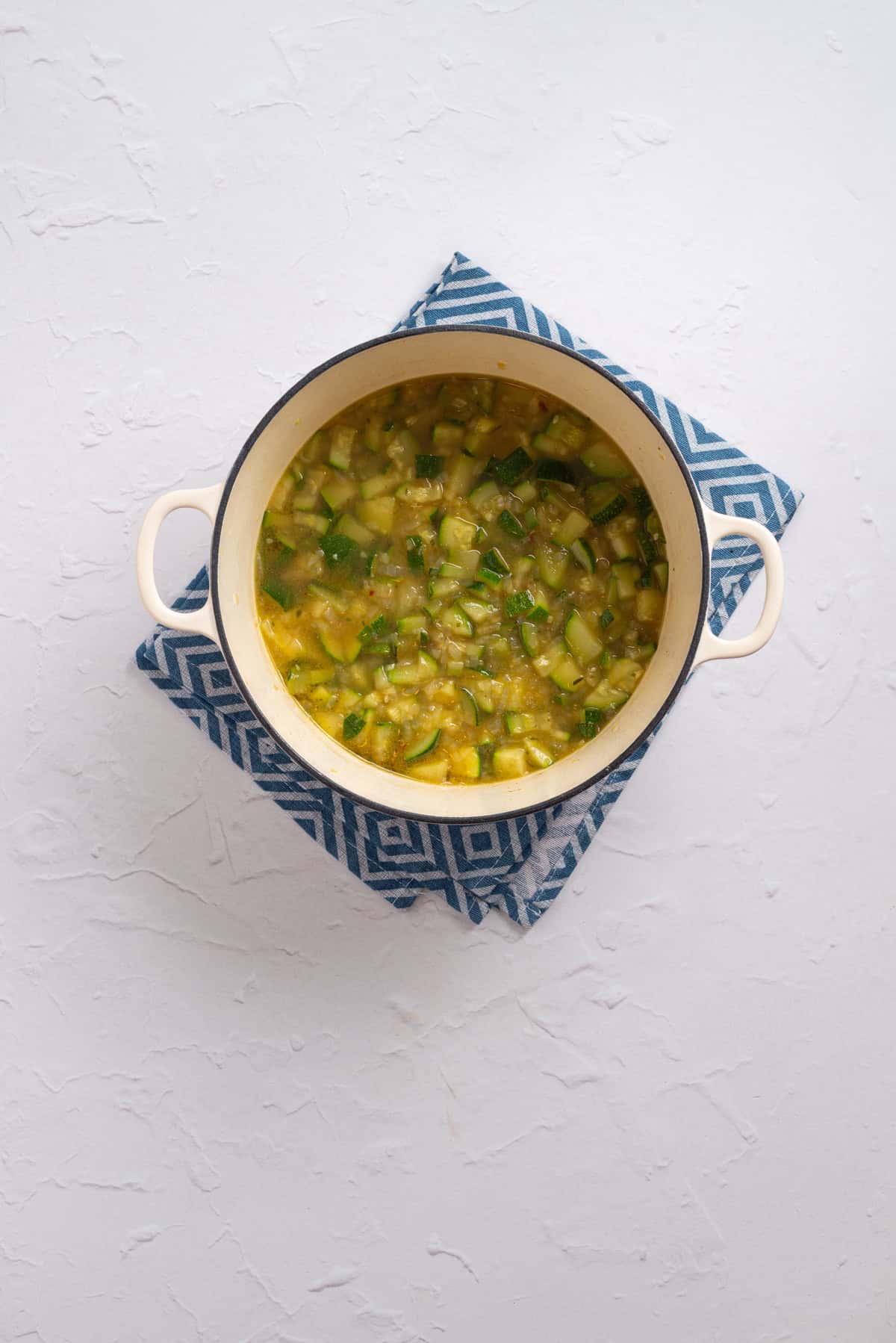 An overhead image of soft , cooked zucchini in the soup mixture.