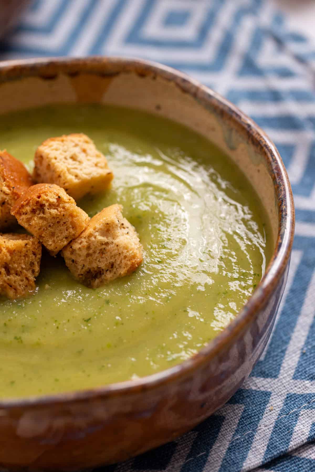 A close up image of zucchini soup with croutons on top.